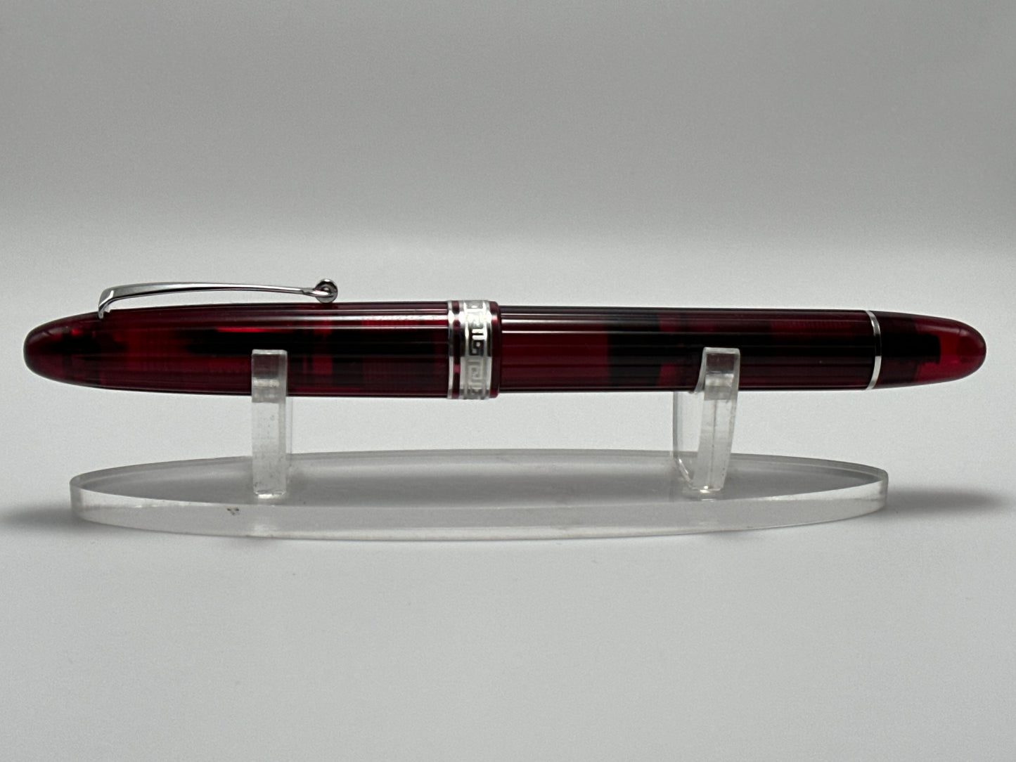 Fountain pen with a maroon and silver design on a clear stand against a gray background