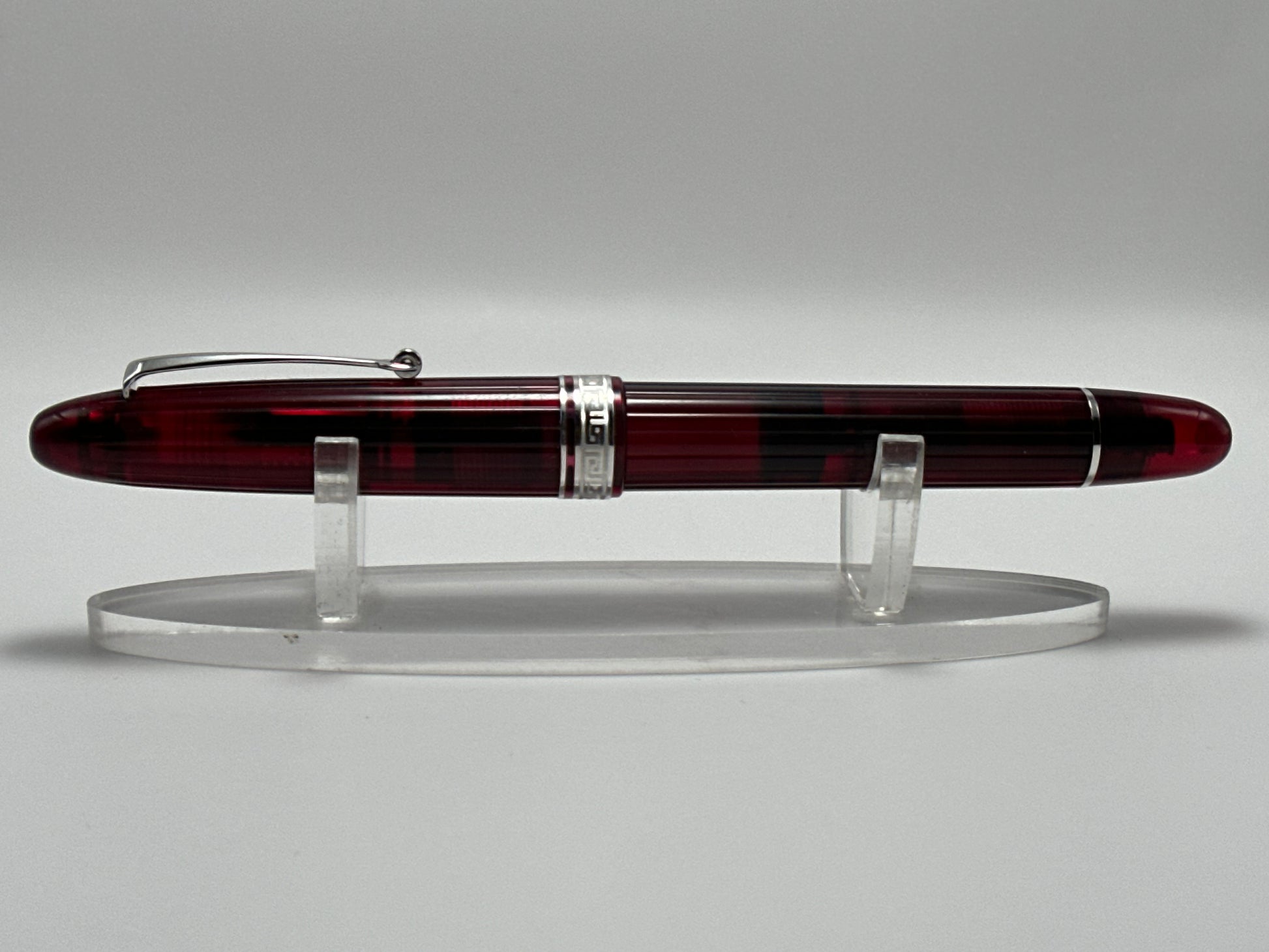 Fountain pen with a maroon and silver design on a clear stand against a gray background