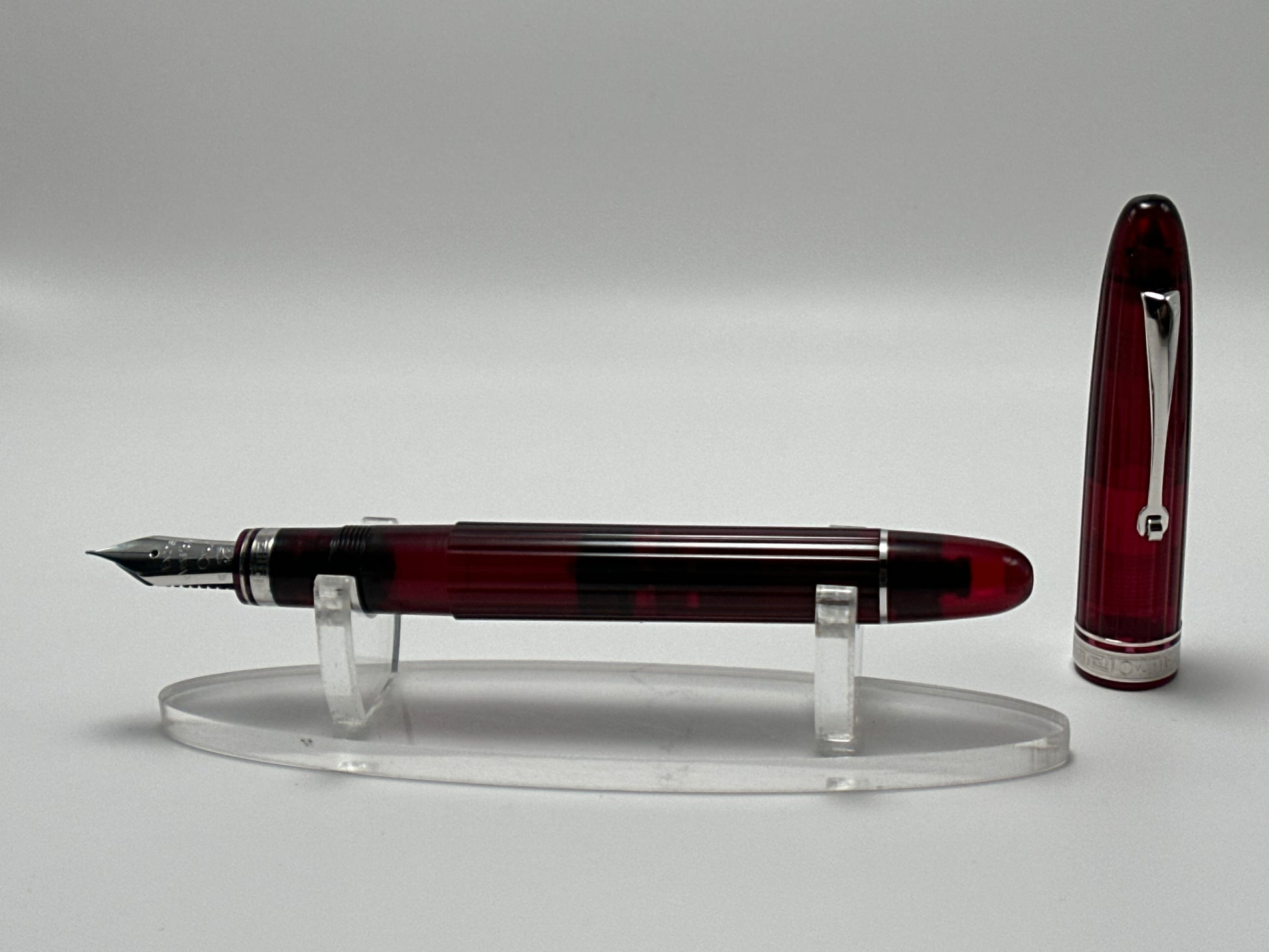 Fountain pen with a red and silver design on a clear stand against a gray background