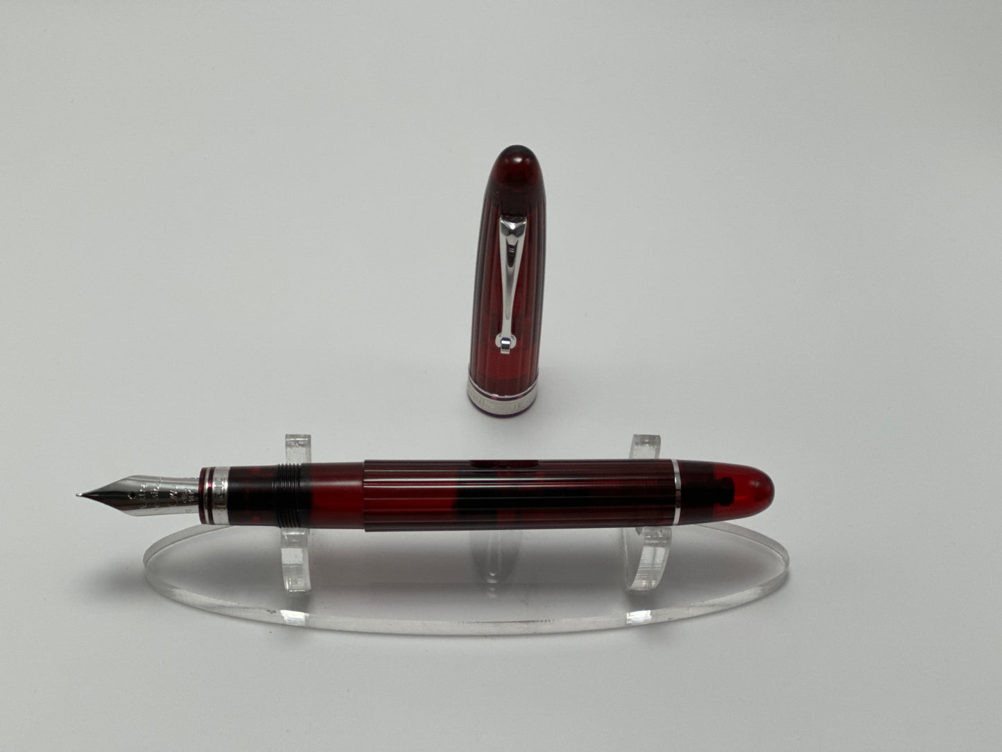 Red and silver fountain pen on a clear stand against a gray background