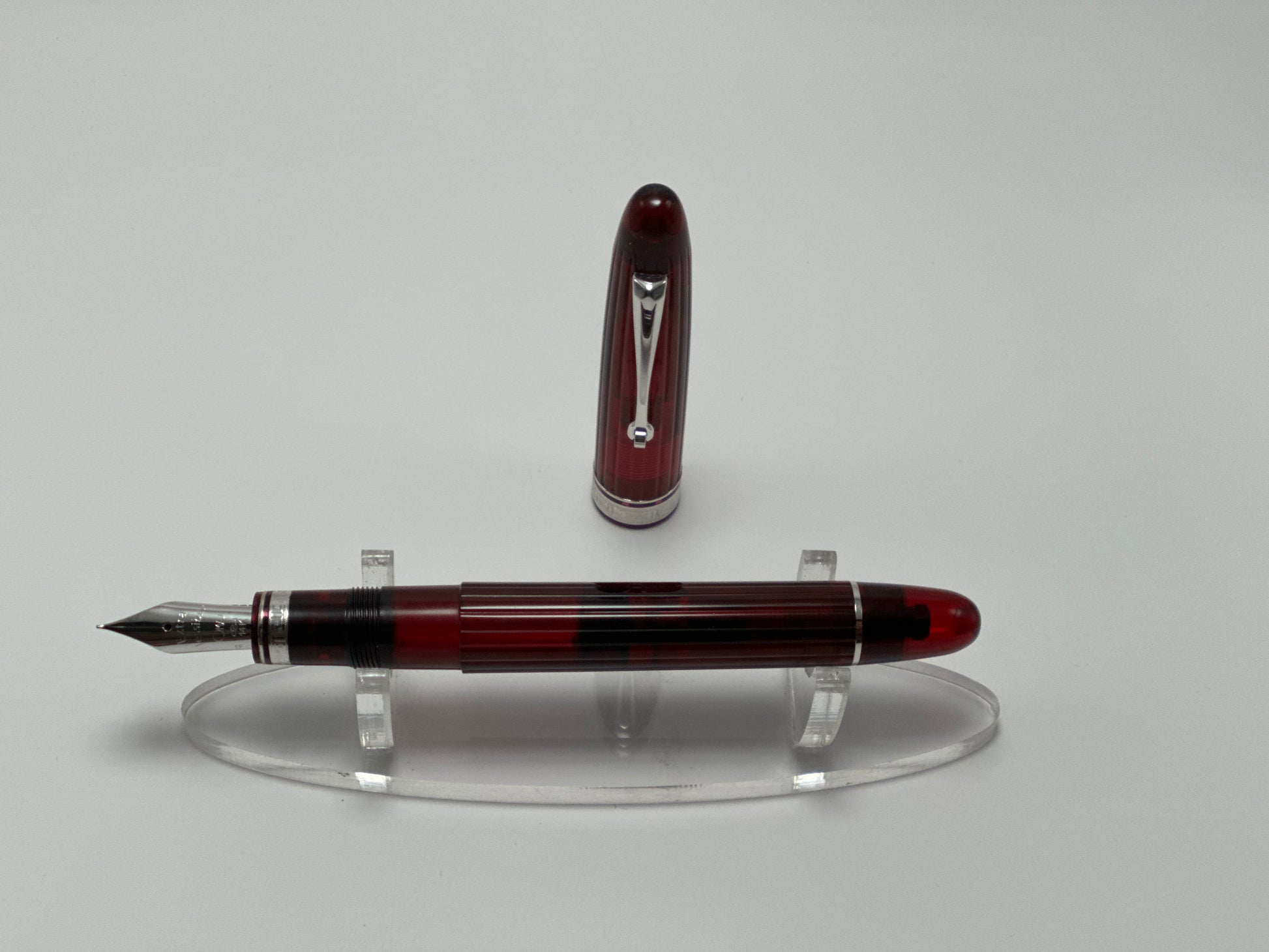 Red and silver fountain pen on a clear stand against a gray background