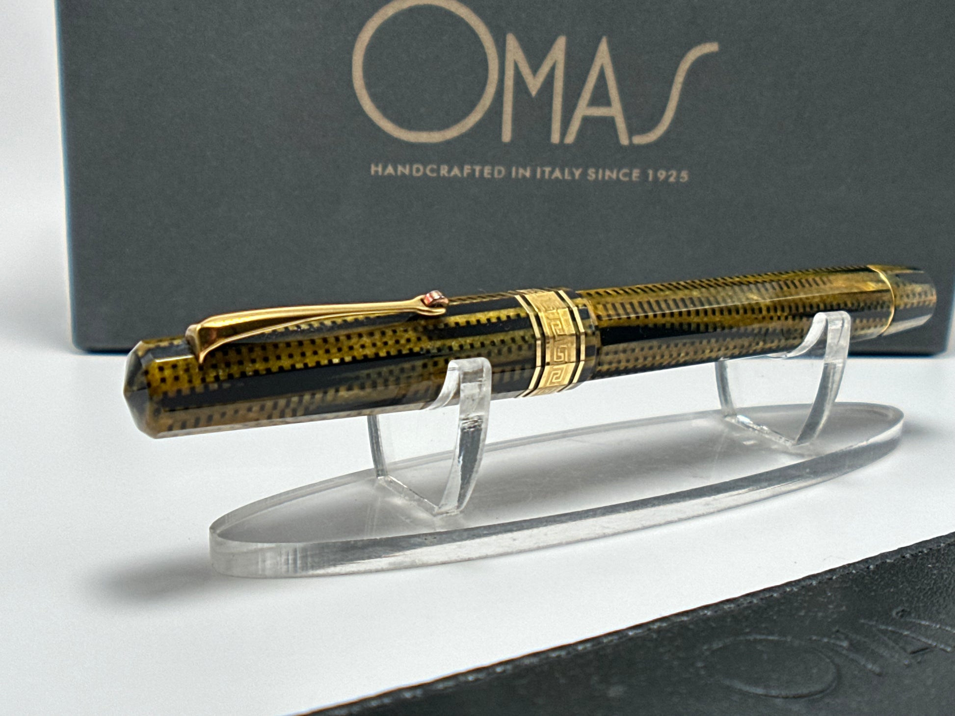 Gold and black pen on a stand with OMAS branding in the background